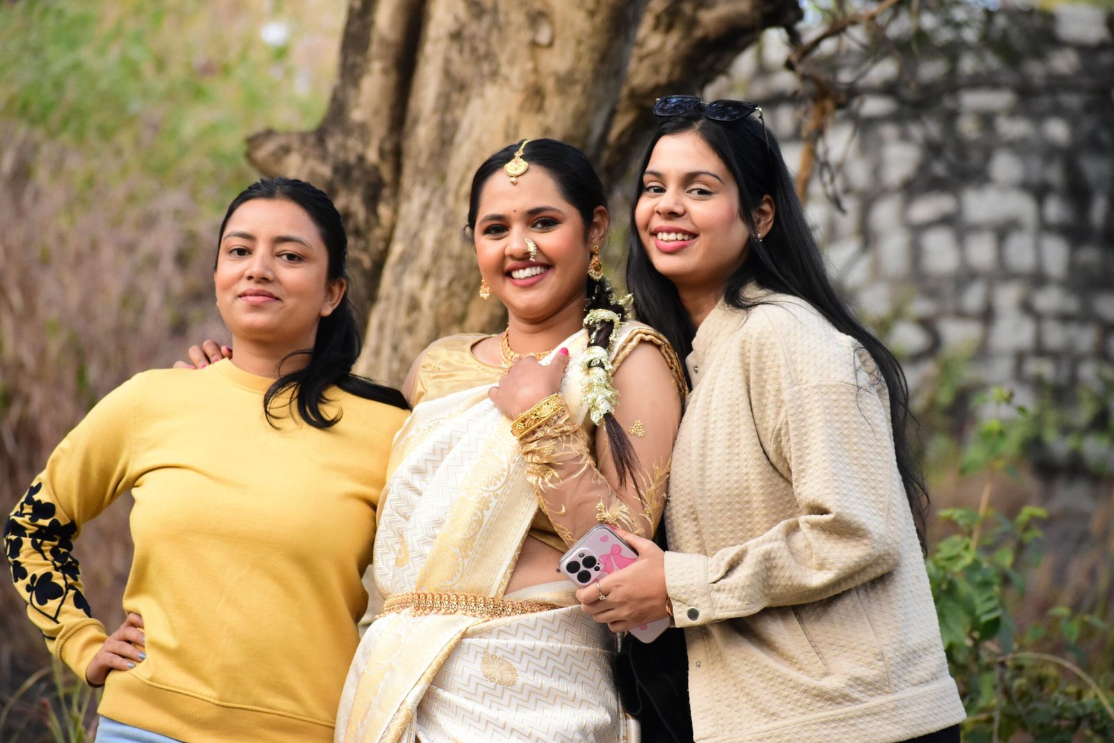 Three women enjoying a day outdoors, with one in bridal attire, smiling for the camera.